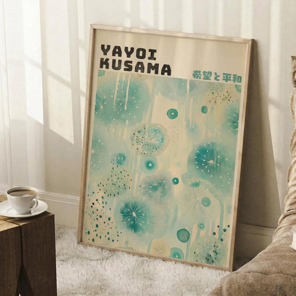 May include: Framed exhibition poster with cream background featuring abstract teal and turquoise dots, circles, and radiating patterns. Black text at top reads "YAYOI KUSAMA" with Japanese characters. Poster leans against white wall corner next to wooden side table with white coffee cup and saucer. Beige textured rug and neutral fabric visible in cozy interior setting with natural window lighting.