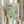 May include: Person in cream sweater holding framed vintage exhibition poster with teal abstract polka dot pattern against cream background, displayed alongside dried wheat stems in soft natural lighting