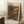 May include: Framed art poster leaning against white wall corner on fluffy white rug. Poster features colorful polka dot pattern with purple, orange, yellow and blue circles on dark background, resembling cosmic or cellular forms. Purple text at top with Japanese characters. Wooden frame, dated 1992. Coffee cup on wooden block nearby, beige blanket visible at right edge.