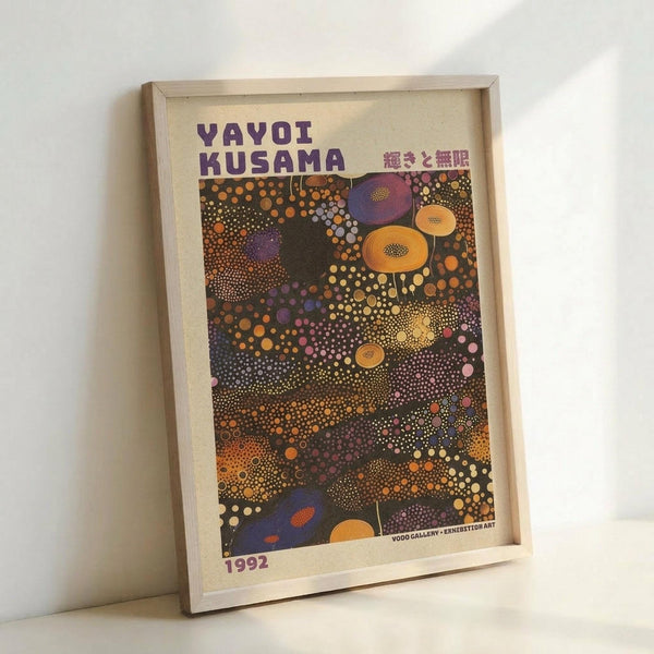 May include: Framed poster featuring Yayoi Kusama's distinctive polka dot artwork in vibrant colors including purple, orange, yellow, and pink circles of varying sizes scattered across a dark background. The print shows "YAYOI KUSAMA" in bold purple letters at the top with Japanese text, dated 1992 at bottom. Light wood frame sits propped against white wall on white surface, creating soft shadows.