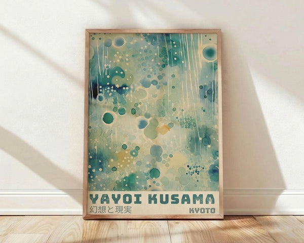May include: Framed art print leaning against white wall on light wood floor. Abstract artwork features dreamy aqua, teal, and cream colors with floating circles, dots, and vertical drips creating an underwater or cosmic effect. Text reads "YAYOI KUSAMA" with Japanese characters and "KYOTO" below. Natural wood frame, soft window light creates shadows on textured white wall.