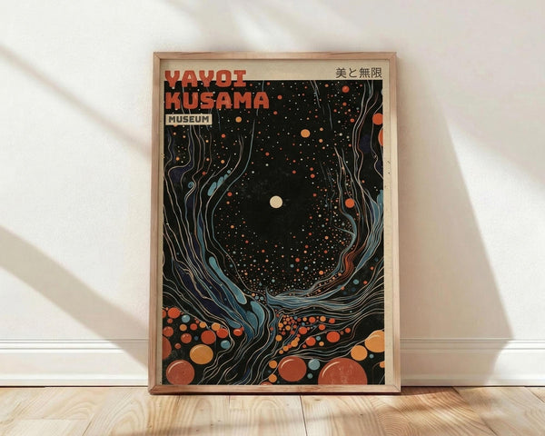 May include: Framed poster print leaning against white wall on light wood floor. Artwork features swirling cosmic design with flowing blue ribbons around black starry center, scattered orange and red circles throughout. White moon or sun in center, Japanese characters in top right corner. Red and black text at top reads "YAYOI KUSAMA MUSEUM". Natural wood frame, soft shadows from window light.