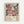 May include: Framed poster with stylized floral pattern in coral, pink, and blue tones against dark navy background, featuring radiating sunburst and circular flower motifs. Text reads "YAYOI KUSAMA" with "JAPAN 1987" and Japanese characters below. Light wood frame mounted on white wall with subtle shadow.