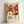 May include: Framed poster with vibrant orange, brown and cream floral pattern featuring stylized flowers, dots and radiating designs in mid-century modern style. Light wooden frame against white wall, showing museum exhibition text with "YAYOI KUSAMA" and Japanese characters, referencing Musée d'Art Moderne de la Ville de Paris.