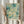 May include: Person holding framed abstract art print with teal and cream watercolor circles, dots, and vertical streaks. Text reads "YAYOI KUSAMA" and Japanese characters below, with "KYOTO" in corner. Natural wood frame, beige clothing, dried pampas grass, soft lighting near white curtained window.