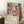 May include: Framed poster with colorful floral pattern featuring coral, pink, and blue flowers on dark navy background, displayed in light wood frame leaning against white wall corner. Coffee cup on wooden surface and beige knit throw visible nearby. Art print shows Japanese text and "JAPAN 1987" at bottom.