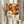 May include: Hands holding a framed art print featuring retro-style floral patterns in warm orange, cream, and brown tones with polka dot accents. Text reads "Yayoi Kusama" with Japanese characters and "Musée d'Art Moderne de la Ville de Paris." Light wood frame against neutral curtained background with dried pampas grass visible on left side.