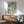 May include: Framed poster with abstract design featuring turquoise and teal polka dots and circles in various sizes scattered across a cream background, displayed above a wooden sideboard in a modern living room. Mid-century style green upholstered armchair with wooden frame sits nearby, with natural sunlight casting shadows on white walls.