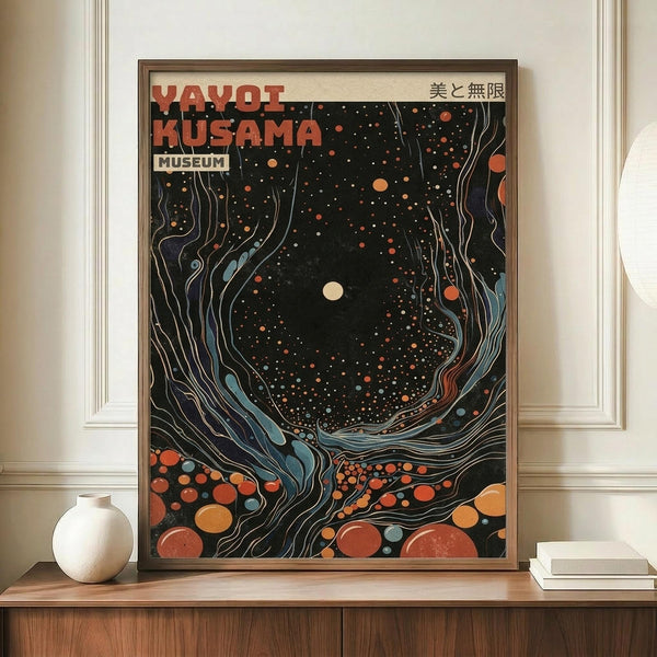 May include: Framed art print with abstract cosmic design featuring swirling patterns in black, orange, red and blue tones with scattered dots and celestial elements, displayed on wooden sideboard next to white ceramic vase and stacked books against cream wall with white trim