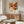 May include: Framed exhibition poster featuring colorful geometric flowers in warm orange, brown, and cream tones displayed above a mid-century modern walnut credenza. Modern living room setting with white curved chair, glass oval coffee table, and brass floor lamp on light wood floors against neutral walls.