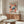 May include: Colorful abstract art poster featuring flowing organic shapes in coral, teal, and navy with dotted patterns, displayed above a mid-century modern walnut credenza in a minimalist living room. White sculptural chair and glass oval coffee table complete the scene with natural lighting casting shadows across polished floors.