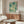 May include: Abstract teal and cream poster with scattered dots and circles in wooden frame, displayed above walnut credenza in modern living room with white curved chair, glass coffee table, and warm natural lighting from window