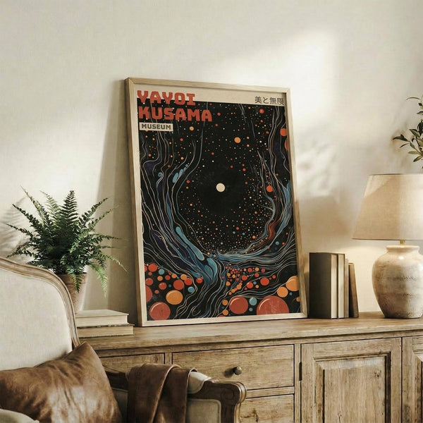 May include: Framed poster with abstract cosmic design featuring swirling patterns in dark background with orange and red circular dots, displayed on rustic wooden console table alongside potted fern, books, and ceramic vase in neutral-toned living room setting with beige armchair visible.