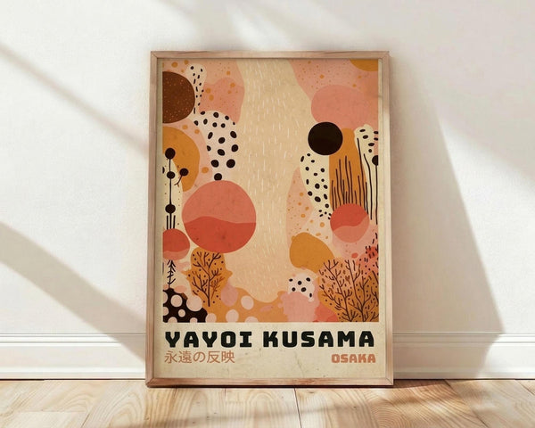 May include: Framed abstract art print leaning against white wall on light wood floor. The poster features warm earth tones with coral, orange, brown and cream organic shapes, black dots, botanical elements, and flowing patterns. Bold black text reads "YAYOI KUSAMA" with Japanese characters below and "OSAKA" in red. Natural wood frame with soft window light creating shadows on textured white wall background.