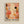 Framed abstract art print featuring warm coral pink, orange, cream and black organic shapes, polka dots, and tree-like patterns in a modern minimalist style. The artwork includes flowing forms, scattered circles, vertical line textures, and botanical silhouettes. Text at bottom reads "YAYOI KUSAMA" with Japanese characters and "OSAKA". Light wood frame displayed against cream colored wall.