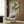 May include: Modern beige armchair with geometric pillow in contemporary living room setting. Framed poster on wood paneled wall features green polka dot pattern with circular motifs and Japanese text. Gold floor lamp and dark round side table with open book visible. Warm wood tones and neutral textiles create minimalist interior design aesthetic.