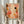 May include: Person holding framed abstract art print with warm autumn colors including peach, coral, orange, and brown geometric shapes, dots, and organic forms. Light wood frame, neutral beige background with dried pampas grass visible to the left. Person wearing cream colored ruffle-sleeve top.