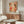 May include: Abstract art poster with warm coral, orange and cream organic shapes, black dots and botanical elements, displayed above a mid-century wooden credenza in a minimalist living room with white curved chair and glass coffee table