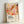 May include: Abstract art poster in light wood frame leaning against white wall. Artwork features flowing organic shapes in warm coral, orange, pink, yellow and burgundy tones with scattered dots throughout. Text reads "YAYOI KUSAMA" in black letters with Japanese characters and "MUSÉE D'ART MODERNE DE LA VILLE DE PARIS" below on cream background.