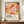 May include: Framed poster with abstract organic shapes in warm coral, orange, pink, and burgundy tones with scattered dots, displayed on wooden sideboard next to white ceramic vase and stacked books against cream wall with white molding