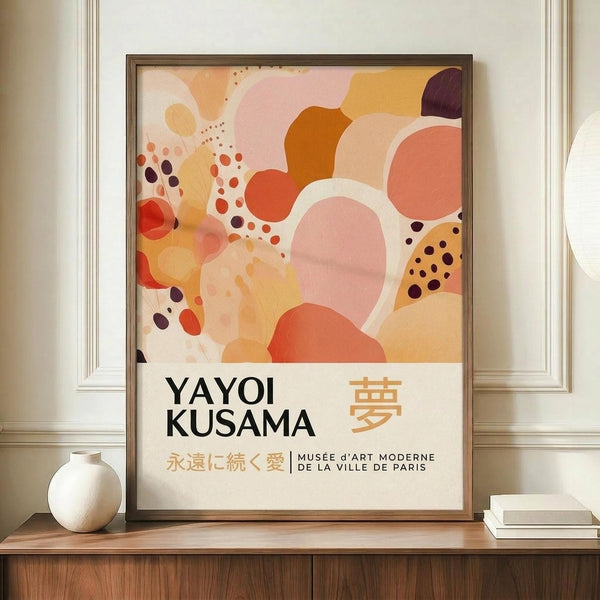 May include: Framed poster with abstract organic shapes in warm coral, orange, pink, and burgundy tones with scattered dots, displayed on wooden sideboard next to white ceramic vase and stacked books against cream wall with white molding