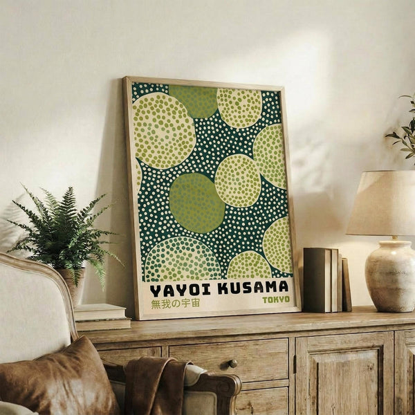 May include: Framed art print with green and cream polka dot circles on dark teal background, displayed on rustic wooden sideboard next to fern plant, books, and ceramic vase in neutral-toned living room setting with beige upholstered chair.