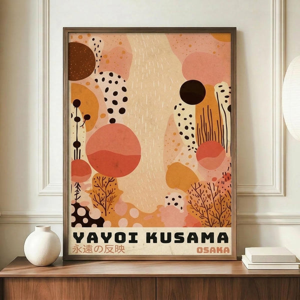 May include: Framed abstract art poster with warm pink, orange, and cream organic shapes, black dots, botanical elements, and Japanese text, displayed on wooden sideboard next to white ceramic vase and stacked books in modern interior with white paneled walls.