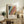 May include: Framed vintage-style exhibition poster with abstract colorful artwork featuring flowing patterns in black, blue, yellow, pink and orange, displayed on rustic wooden sideboard alongside fern plant, ceramic vases, and stacked books in neutral-toned living room setting