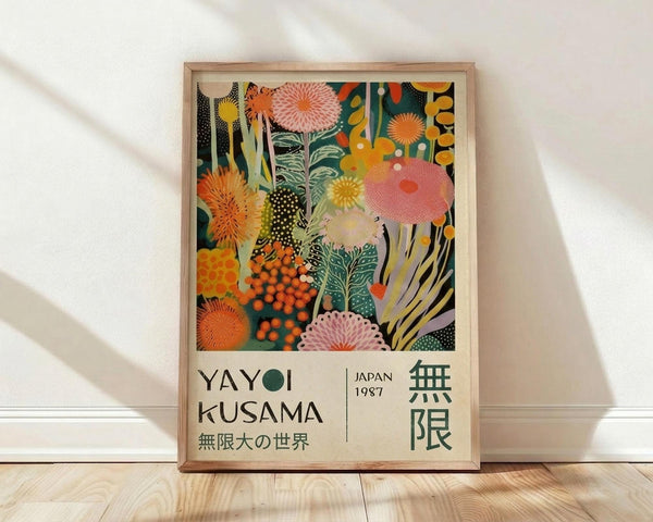 May include: Framed art print leaning against white wall on light wood floor. Colorful abstract botanical design with coral, orange, yellow and teal circular flowers, mushrooms and organic shapes in layered collage style. White mat border with "YAYOI KUSAMA" and "JAPAN 1987" text below artwork. Natural wood frame. Soft window light casting shadows across white textured wall.