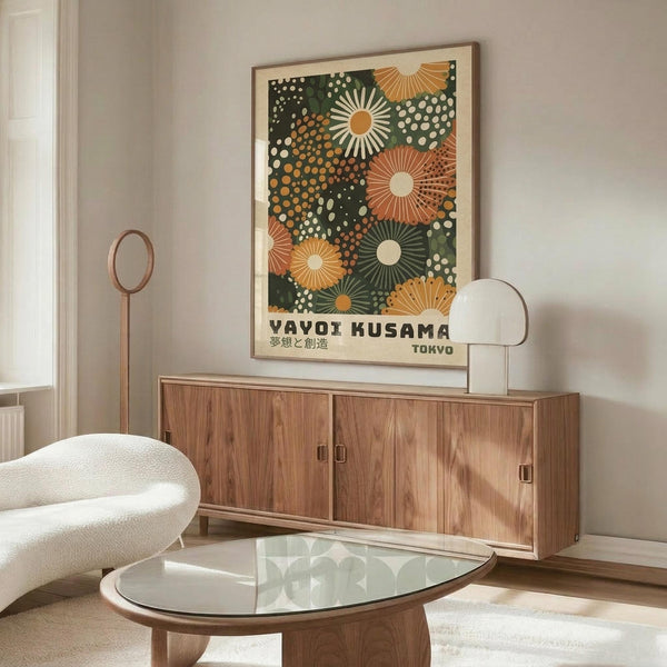 May include: Framed art print hanging above wooden credenza in modern living room setting. Print features colorful sunburst and dot pattern in green, orange, and cream tones with Japanese text. White sculptural chair and glass coffee table visible in foreground. Warm natural lighting illuminates the minimalist space with neutral walls.