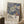 May include: Framed art print leaning against white wall featuring stylized flowers in muted green, coral, and white tones against deep blue dotted background, with Japanese text below. Natural lighting creates soft shadows. White coffee cup on wooden surface and textured throw blanket visible nearby in cozy interior setting.