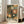 May include: Framed art print with dark green background featuring radiating sunburst patterns and polka dots in orange, cream, and green tones. Japanese text at bottom reads "YAYOI KUSAMA" with characters and "TOKYO". Print displayed in light wood frame leaning against white wall next to beige sofa in bright room with large windows.