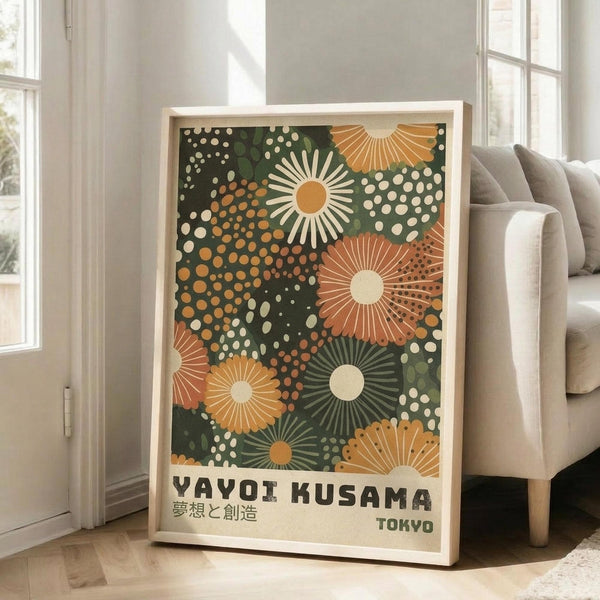 May include: Framed art print with dark green background featuring radiating sunburst patterns and polka dots in orange, cream, and green tones. Japanese text at bottom reads "YAYOI KUSAMA" with characters and "TOKYO". Print displayed in light wood frame leaning against white wall next to beige sofa in bright room with large windows.