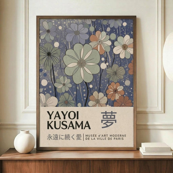 May include: Framed art poster featuring stylized flowers in soft blues, greens, peaches and cream colors against a dotted background, with "YAYOI KUSAMA" text and Japanese characters below. Displayed on wooden sideboard next to white ceramic vase and stacked books in neutral-toned room with white walls and crown molding.
