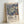 May include: A framed art print leaning against a white wall, featuring stylized flowers in soft greens, purples, and coral tones against a deep blue dotted background. The print shows "YAYOI KUSAMA" and Japanese characters at the bottom, along with "MUSEE D'ART MODERNE DE LA VILLE DE PARIS." The natural wood frame has a light finish and the overall composition has a modern, museum poster aesthetic.