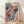 May include: Framed poster print leaning against white wall on light wooden floor. Light wooden frame contains colorful abstract artwork with flowing organic shapes, polka dots, and swirling patterns in navy blue, coral orange, teal, and cream. Text reads "YAYOI KUSAMA" with Japanese characters and "1991" at bottom. Natural sunlight creates soft shadows on white textured wall behind frame.
