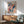 May include: Colorful abstract art poster with flowing organic shapes in orange, blue, and coral tones, featuring polka dot patterns and wave-like forms. Displayed in wooden frame above mid-century modern credenza with white ceramic lamp. Mint green upholstered armchair with wooden arms sits nearby on wooden floor with natural sunlight creating geometric shadows on white wall.