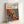 May include: Framed art print leaning against white wall featuring Yayoi Kusama's signature polka dot pattern in vibrant orange, yellow, blue and red organic shapes with black oval spots throughout. Text reads "YAYOI KUSAMA" at top with Japanese characters and "JAPAN 1987" below. Natural wood frame, white matting, positioned on light surface with soft shadows.
