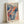 May include: Framed poster print featuring abstract artwork with flowing ribbons in blue, coral, and teal alongside scattered polka dots in various sizes and colors. Text reads "YAYOI KUSAMA" in bold navy letters with Japanese characters and "1991" at bottom. The colorful design combines organic wavy streams with geometric dot patterns against a cream background. Displayed in light wood frame leaning against white wall.