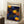May include: Framed poster with blue background featuring yellow and orange polka dots in various sizes, three prominent yellow circular swirl motifs, and black text "YAYOI KUSAMA" with Japanese characters and "KYOTO" in orange. Light wood frame leaning against white wall corner next to white coffee cup on wooden block and cream textured blanket on white fluffy rug.