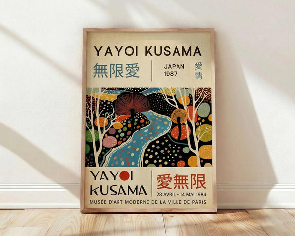 May include: Framed exhibition poster featuring Yayoi Kusama's colorful abstract artwork with polka dots, organic shapes, and vibrant patterns in blues, oranges, and earth tones. Text shows "YAYOI KUSAMA" with Japanese characters, "JAPAN 1987" and museum exhibition details. Natural wood frame leaning against white wall on light wooden floor with soft natural lighting creating gentle shadows.