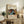 May include: Framed vintage-style exhibition poster featuring Yayoi Kusama artwork with colorful polka-dotted abstract shapes, trees, and organic forms in blues, reds, yellows, and greens. Text in Japanese and French indicates museum exhibition dates. Poster displayed on rustic wooden sideboard alongside fern plant, ceramic vase, books, and cream upholstered furniture in neutral-toned living room setting.