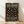 May include: Framed poster with black background and colorful polka dots in muted earth tones including coral, sage green, cream, and golden yellow scattered across the surface. White text displays artist name and exhibition details. Wooden frame leans against white wall on light wood flooring with soft natural lighting creating diagonal shadows.