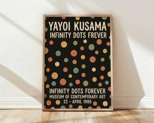 May include: Framed poster with black background and colorful polka dots in muted earth tones including coral, sage green, cream, and golden yellow scattered across the surface. White text displays artist name and exhibition details. Wooden frame leans against white wall on light wood flooring with soft natural lighting creating diagonal shadows.