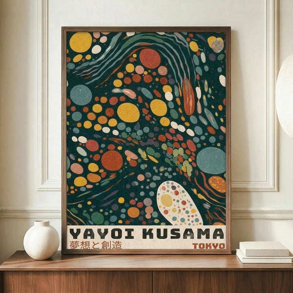 May include: Framed art print displayed on wooden sideboard featuring abstract design with dark teal background filled with colorful circles, dots, and flowing patterns in yellow, orange, red, and blue. Text reads "YAYOI KUSAMA" with Japanese characters and "TOKYO" below. White ceramic vase and stacked books sit alongside the medium-sized framed poster against cream colored walls with white molding.