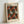 May include: Framed art print in light wood frame leaning against white wall. Features abstract pattern of red and white polka-dotted organic shapes resembling mushrooms or shells on black dotted background. Text reads "YAYOI KUSAMA" and "INFINITY SHELL" at top, Japanese characters and "1970" at bottom. Vintage exhibition poster style with cream-colored paper background.