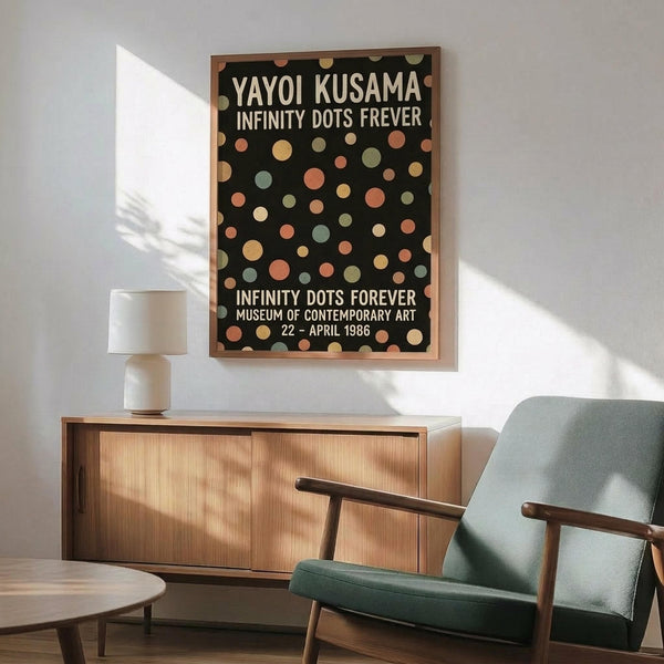 May include: Framed poster with black background and colorful polka dots in muted tones of coral, sage green, cream, and peach, displayed above a wooden sideboard with white ceramic lamp. Mid-century modern teal upholstered chair with wood arms sits beside small round coffee table. Warm natural lighting creates shadows on white wall in minimalist living room setting.