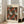 May include: Framed poster with orange and white polka-dotted shell shapes scattered across a dark spotted background, displayed in light wooden frame leaning against white wall next to beige upholstered chair in bright room with large windows