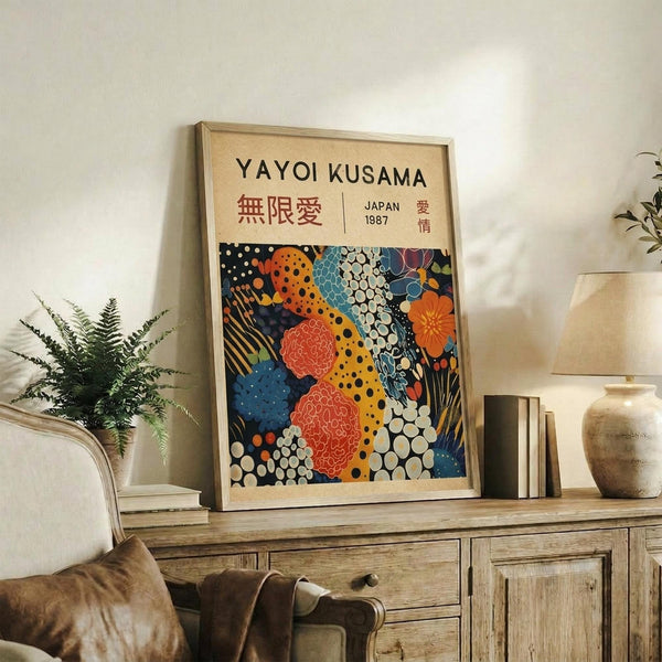 May include: Framed art poster with colorful abstract pattern featuring orange, red, blue, and black organic shapes with polka dots and geometric designs, displayed on rustic wooden sideboard next to fern plant, books, ceramic vase, and cream upholstered chair in neutral living room setting