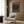 May include: Framed exhibition poster featuring colorful polka dots on black background displayed on wood paneled wall above beige armchair with geometric throw pillow, brass floor lamp and side table with open book nearby, warm neutral modern interior setting